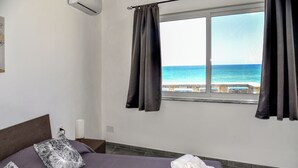 Une chambre à coucher avec un lit, des oreillers, une fenêtre avec des rideaux et une vue sur la mer.