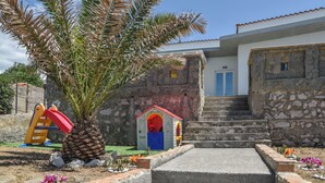 Un bâtiment en pierre avec une porte rouge, une petite maison de jeu et un palmier.