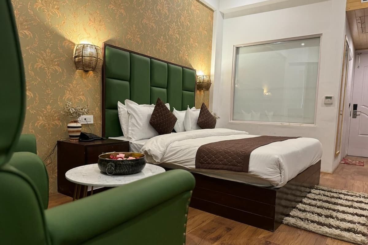 Un dormitorio con un cabecero tapizado en verde, una cama con ropa de cama blanca y marrón, una mesita de noche con un frutero, y un ventanal grande.
