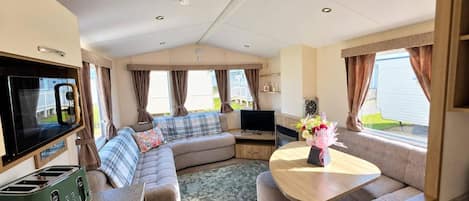 A compact RV interior with a sofa, TV, kitchenette, and a dining area.