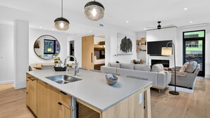 Une cuisine moderne dotée d’un îlot central, un coin repas avec un canapé et un salon avec une télévision et une cheminée.