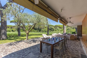 Eine Terrasse im Freien mit Tisch und Stühlen, umgeben von Steinböden und Bäumen.
