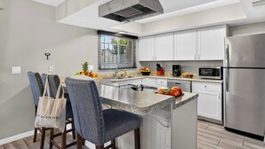 Uma cozinha moderna com ilha central, eletrodomésticos de aço inoxidável e uma janela com persianas.