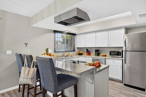 A modern kitchen with a central island, stainless steel appliances, and a window with blinds. - 4BR + BBQ Patio + Bunk Room + Community Pool | Walk to Old Town | Saguaro Social (Scottsdale)