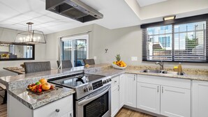 Uma cozinha moderna com ilha central, eletrodomésticos de aço inoxidável, uma grande janela com persianas e vista para o exterior.