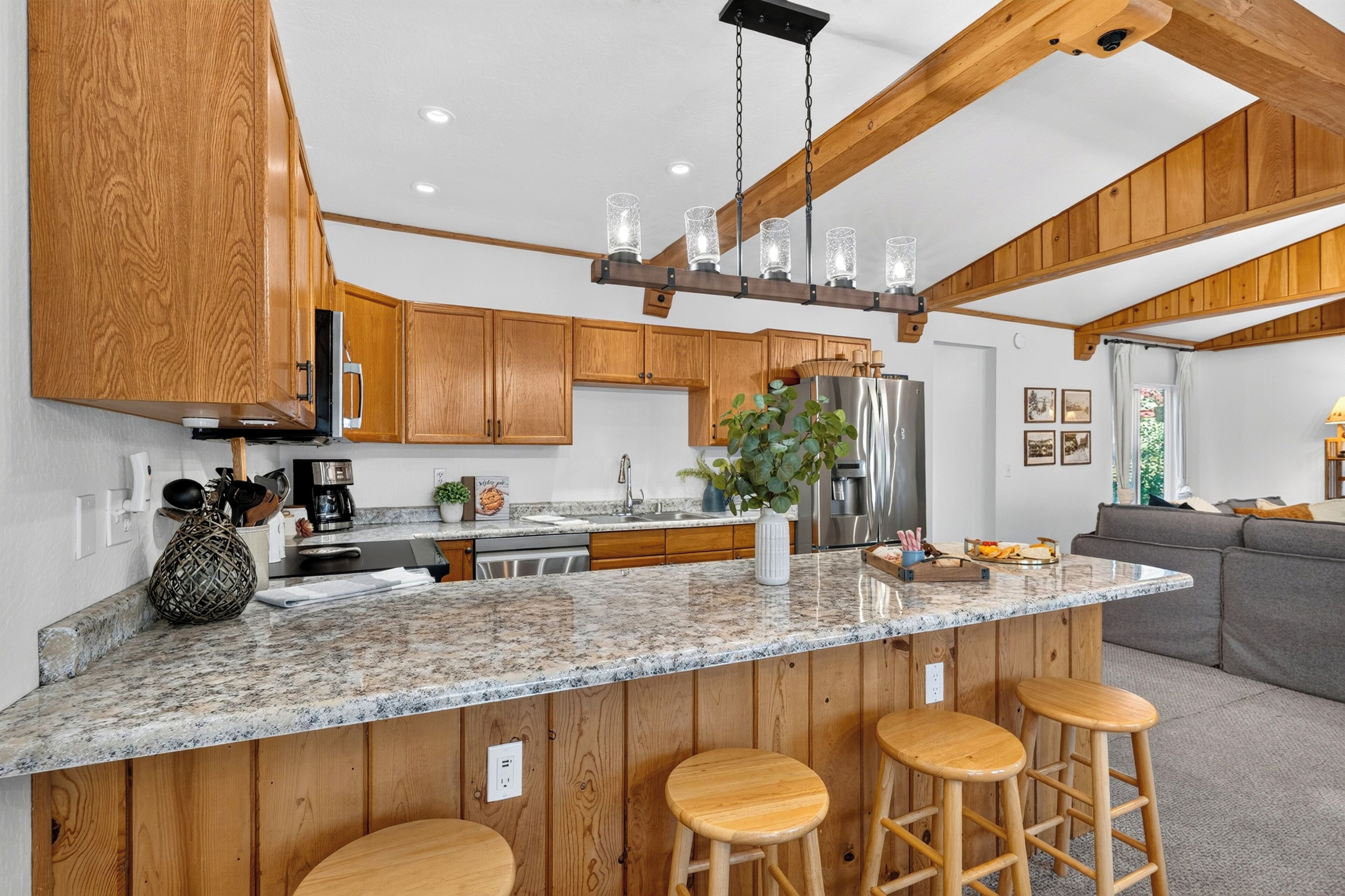 Cocina con gabinetes de madera, encimera de granito y lámpara colgante.
