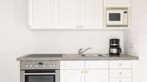 A kitchen with white cabinetry, a granite countertop, a built-in oven, a microwave, a sink, and a coffee maker. - Charming House with Garden Access (Wien)