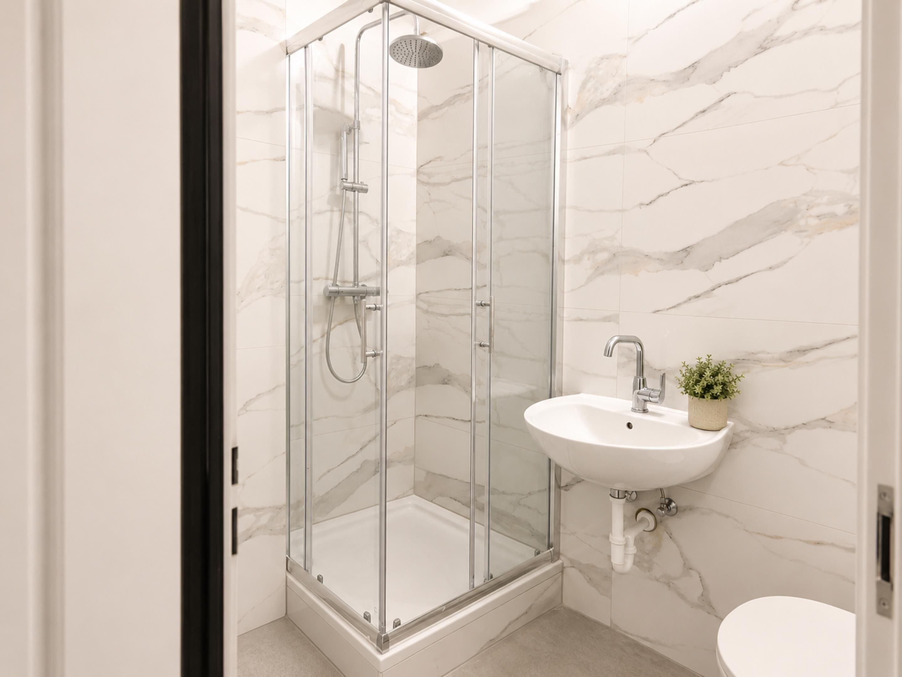 A modern bathroom with a glass-enclosed shower, a white sink, and a marble wall.
