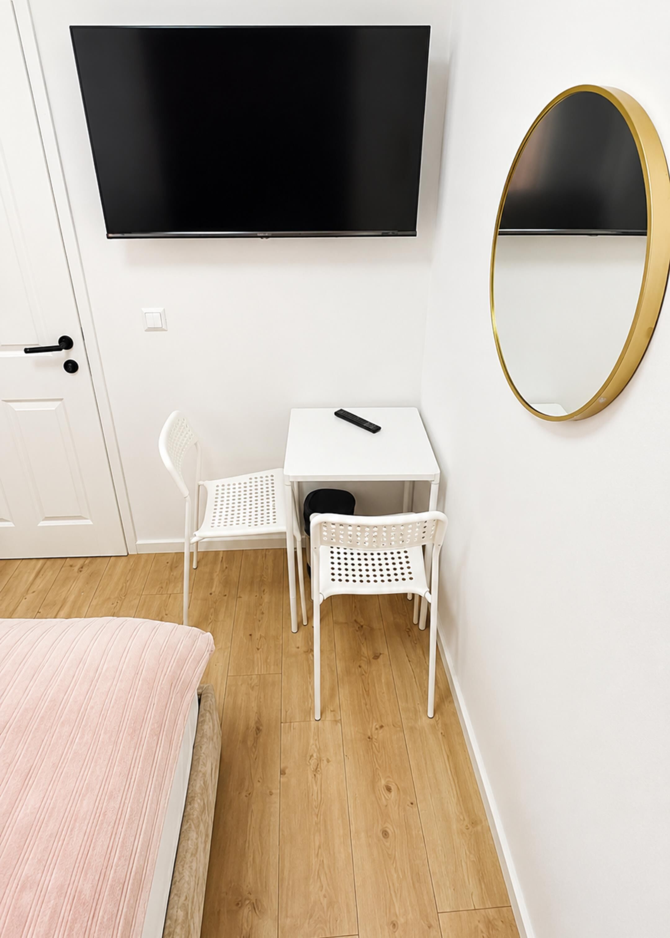 Ett rum med en säng, ett litet bord med två stolar, en tv och en spegel.