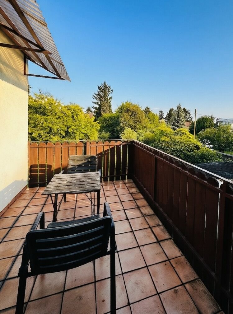 En balkon med flisegulv, et træhegn og udsigt til grønt.