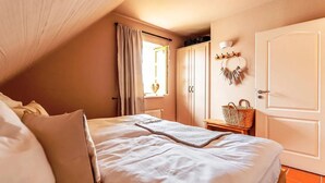 Une chambre à coucher avec un lit, une fenêtre avec des rideaux, une armoire et un luminaire fixé au mur.