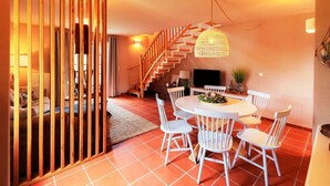 Un coin repas avec une table ronde, des chaises blanches, un téléviseur et un escalier.