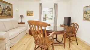 A living room with a sofa, wooden chairs, a glass-top table, a TV, and paintings on the walls. - Surfer's Paradise Wiek - Lee Vacation Rental (Wiek)
