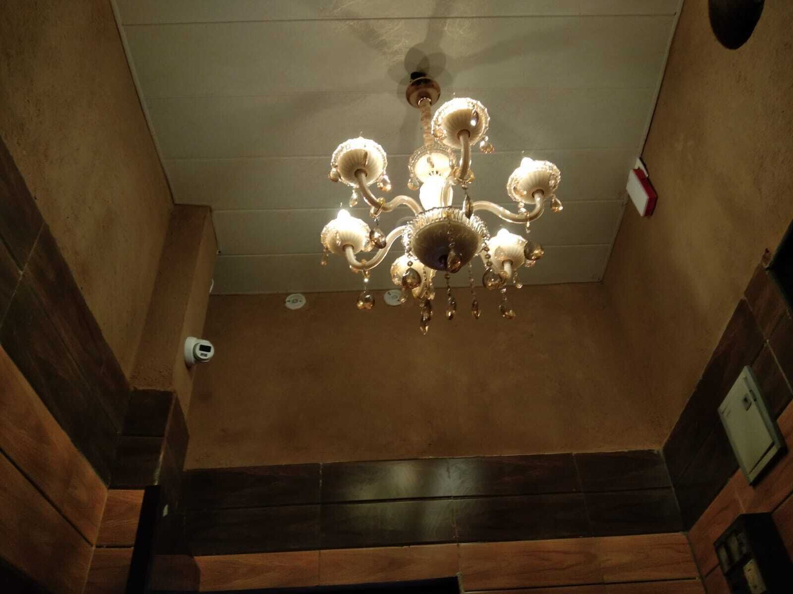 A chandelier with multiple arms and light fixtures, a wooden wall panel, and a door at the bottom.