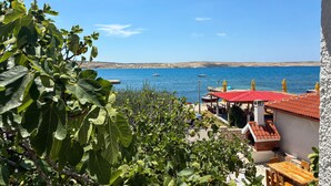 A coastal view with a clear sky, a beach with umbrellas, and a building with a red roof. - Cozy apartment in Kustici with WiFi (Kustici)