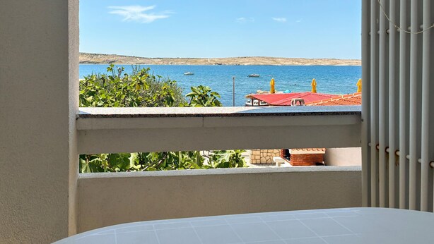 A balcony with a view of the sea, a boat, and a red-roofed building. - Cozy apartment in Kustici with WiFi (Kustici)