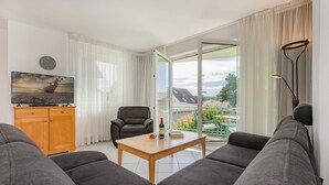 Een moderne woonkamer met een bank, een houten salontafel, een televisie en een fauteuil.