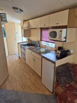 Una kitchenette compacta con estufa, microondas, pileta y un refrigerador pequeño.