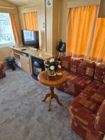 Una sala de estar acogedora con sofá, televisor, una mesita con un jarrón de flores y un ventilador.