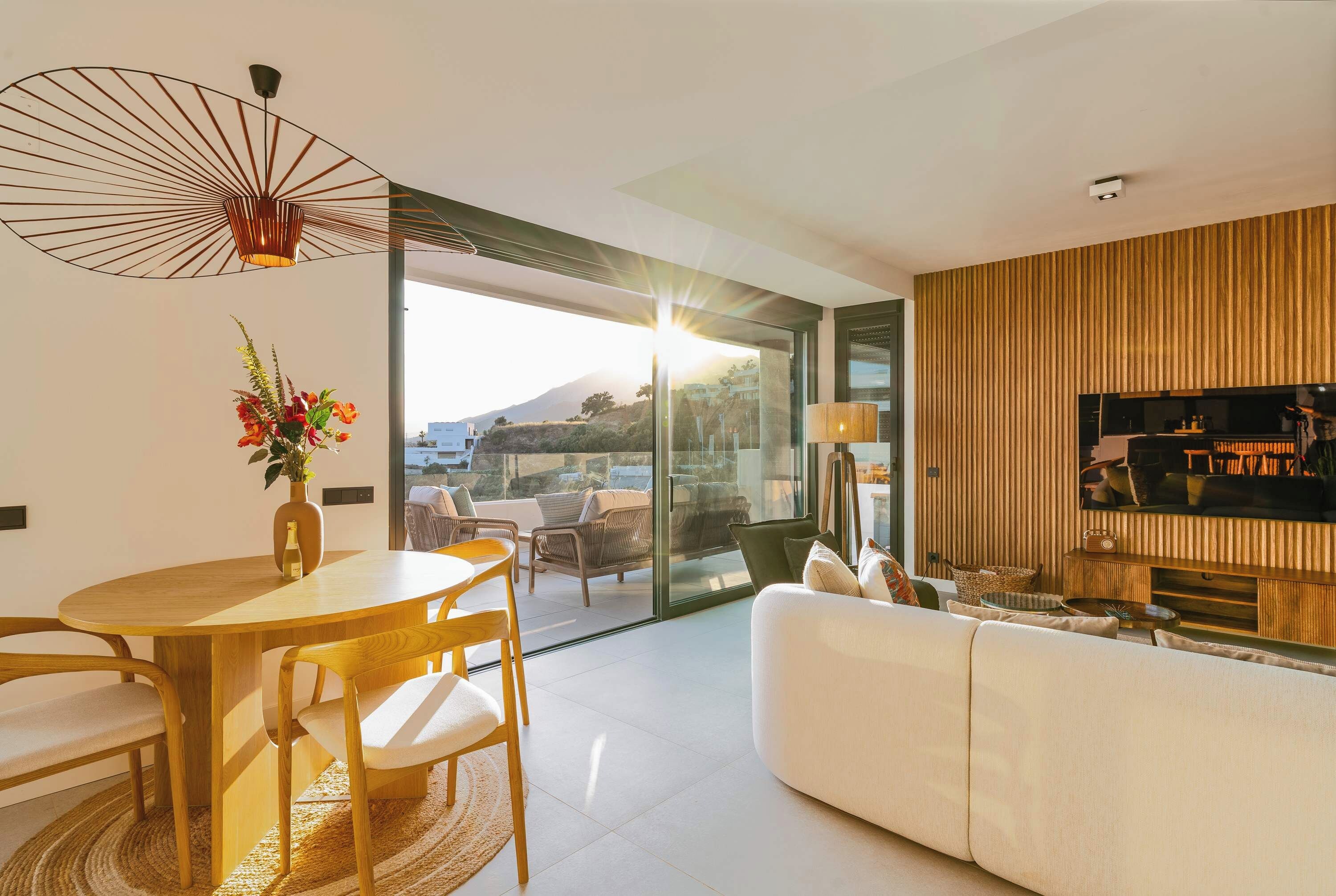 A modern living room with a dining area, a sofa, a TV, and a view of a mountain.