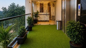 Un balcón con césped artificial, plantas en macetas y un ascensor.