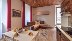 Ein gemütlicher Wohnbereich mit einer Couch, einem Esstisch mit Obst und einer Küche mit Holzschränken.