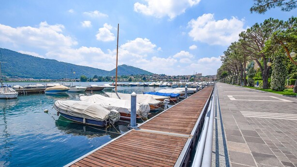 Ein Yachthafen mit vertäuten Booten, einer Holzpromenade und einer Stadtlandschaft im Hintergrund.