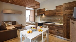 Eine moderne Küche mit Holzschnitzereien, ein Essbereich mit Tisch, gedeckt für eine Mahlzeit, und ein Wohnbereich mit einer Couch.