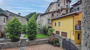 Ein Innenhof mit Steingebäuden, darunter ein gelbes Gebäude mit Balkon, und grünen Bäumen.