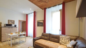 Ein Wohnzimmer mit braunem Ledersofa, einem Esstisch mit Stühlen, einer Küchenzeile mit Mikrowelle und einem roten Vorhang.