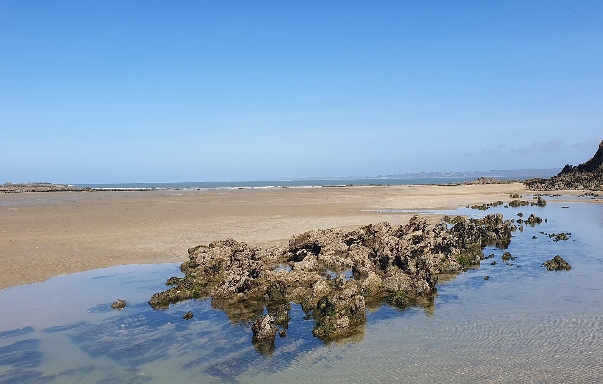 A beach with rocky formations in the water and a clear sky.