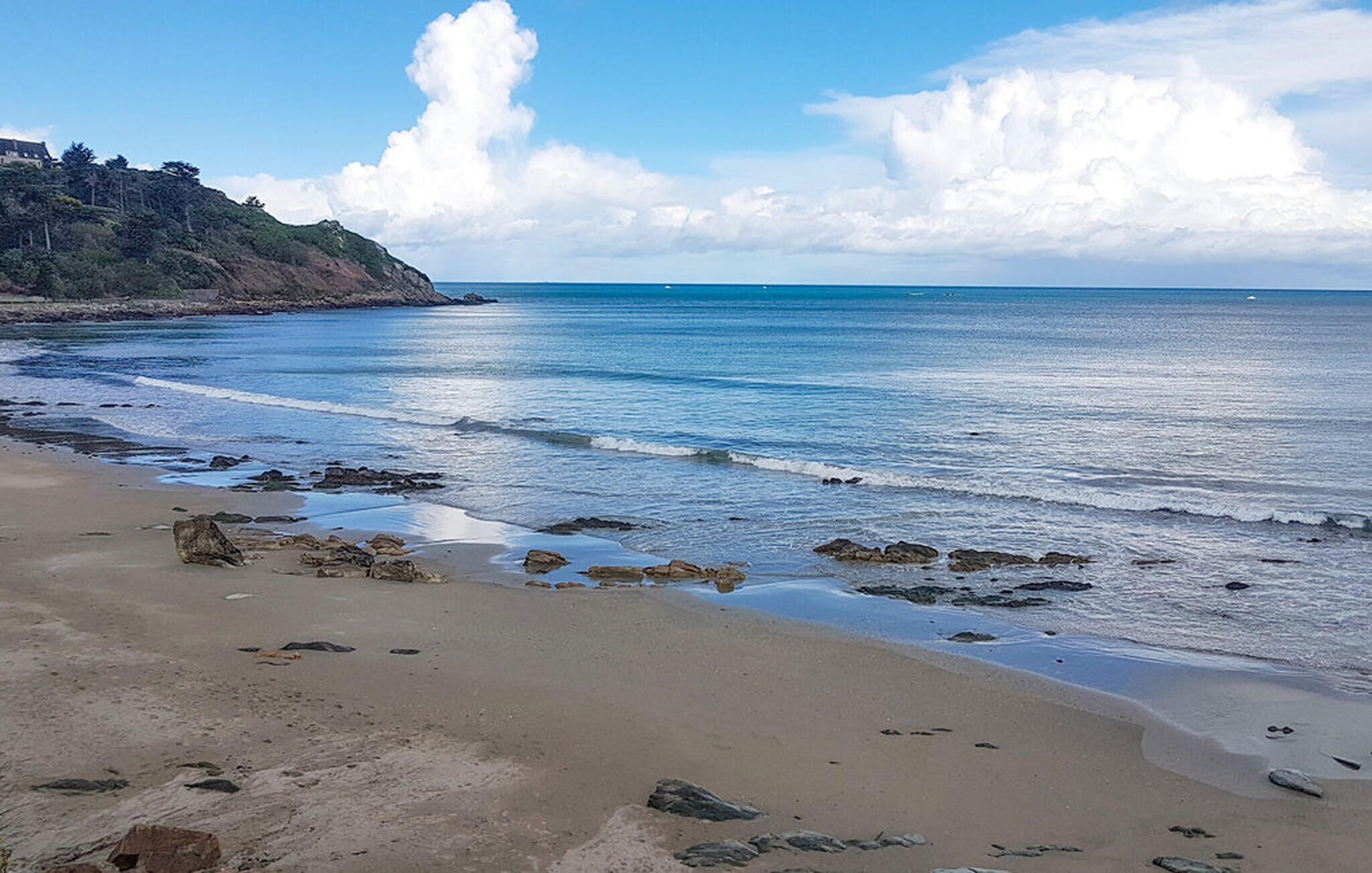 A beach with clear blue water, a sandy shore, and a rocky outcrop.