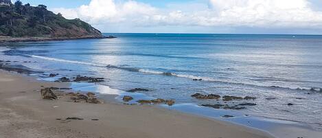 A beach with clear blue water, a sandy shore, and a rocky outcrop.