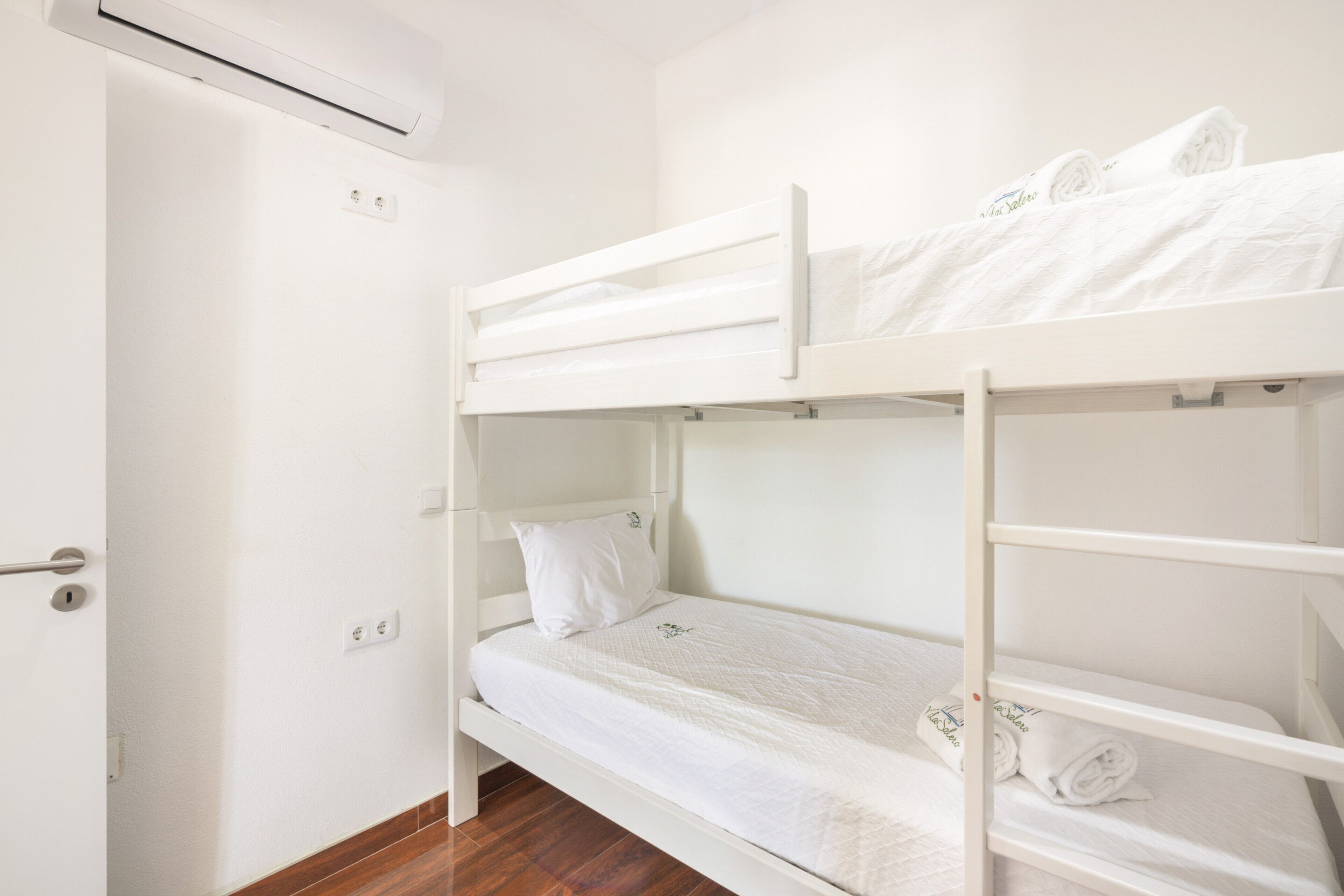 Une chambre avec un lit superposé, une porte, un appareil de climatisation et un plancher en bois.