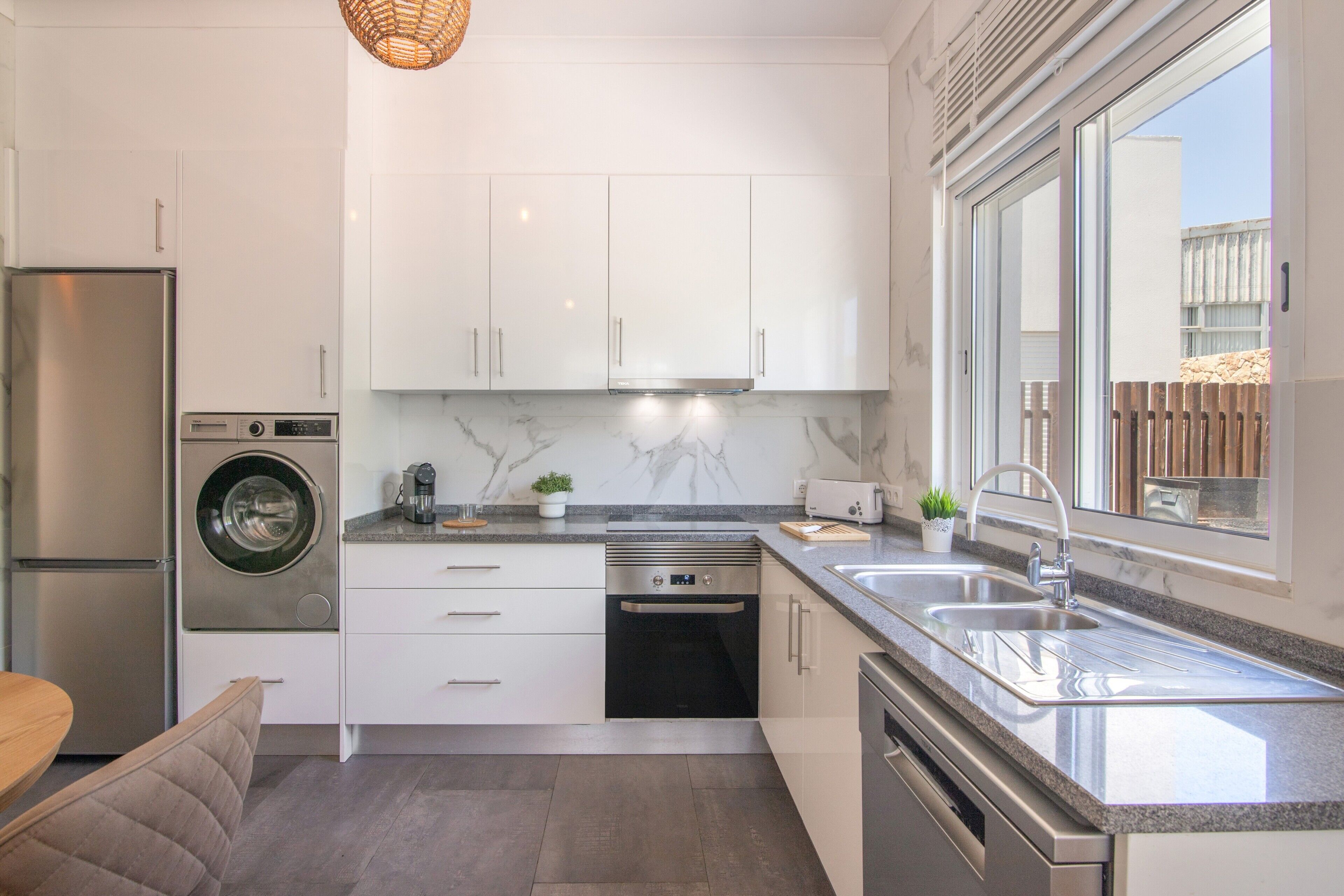 A modern kitchen with a built-in washer, dishwasher, and oven; a large window with a view; and a dining area with a bench.