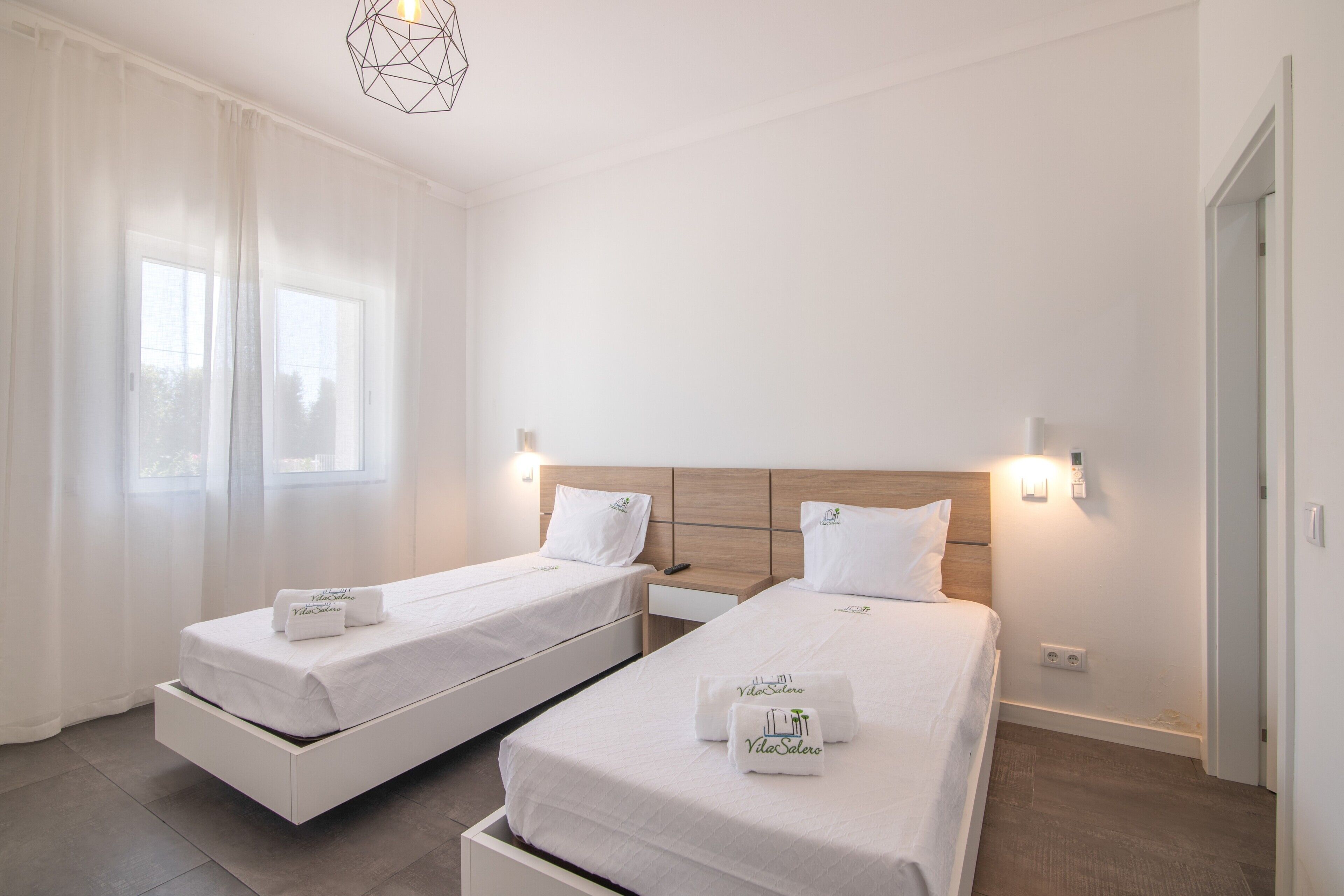 Camera d'albergo con due letti singoli, una testiera in legno, un comodino e una lampada a sospensione moderna.