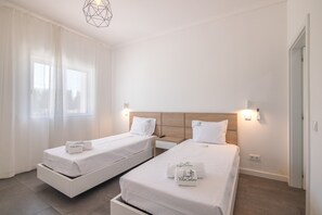 Quarto de hotel com duas camas de solteiro, cabeceira de madeira, mesa de cabeceira e luminária pendente moderna.