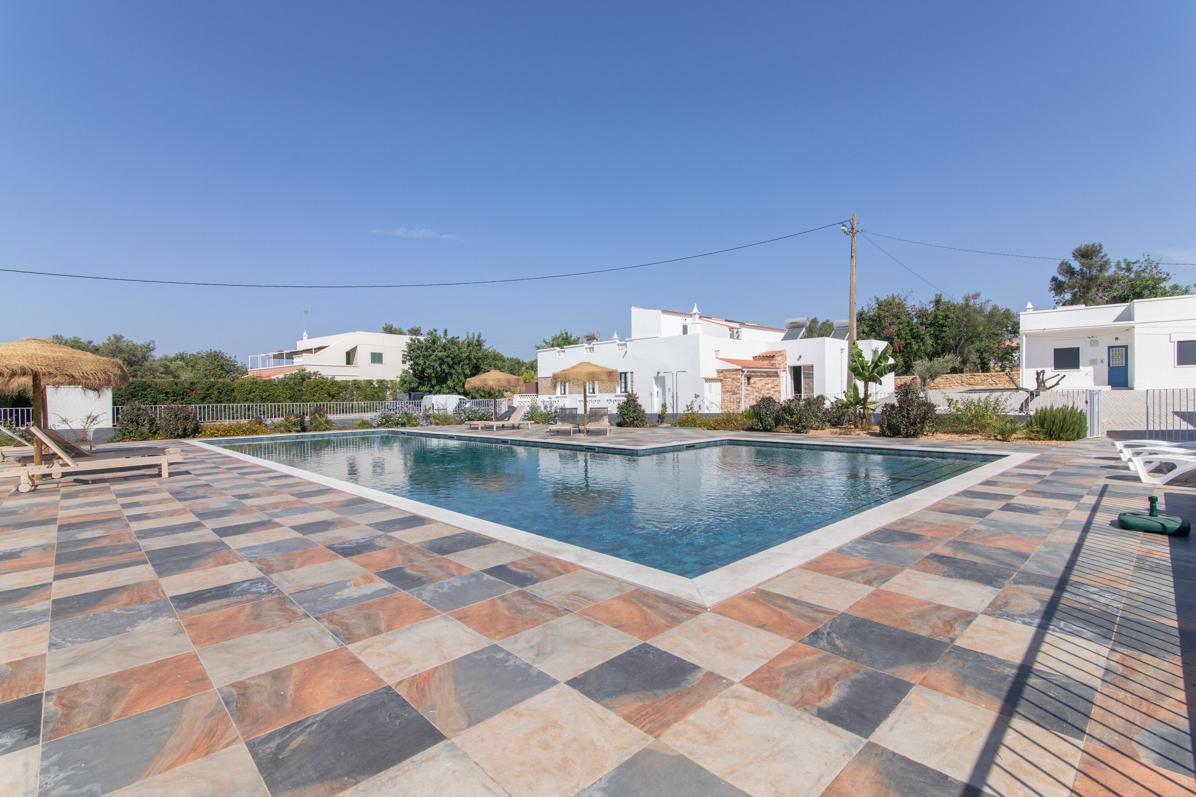 Una piscina con bordo a scacchi, circondata da edifici bianchi con tetti in tegole rosse e un cielo blu limpido.