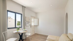 Ein modernes Wohnzimmer mit einem beige farbenen Sofa, einem Esstisch mit Stühlen und Blick ins Freie durch ein großes Fenster.