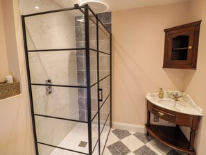 A bathroom with a glass shower enclosure, a marble-tiled floor, a wooden vanity with a sink, and a wooden cabinet above the mirror. - The Stable Flat (Lutterworth)