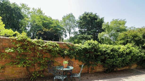 Eine Terrasse mit Backsteinmauer, Tisch und zwei Stühlen.
