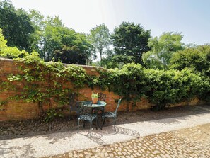 A patio with a brick wall, a table, and two chairs. - The Stable Flat (Lutterworth)