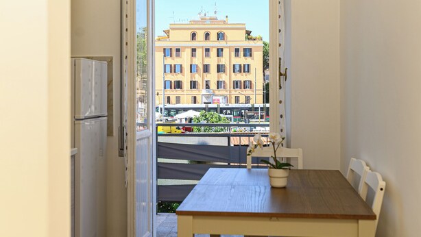A balcony with a view of a building, a table with a chair, and a potted plant. - Appartamento Monteverde Casa Marí Roma (Roma)