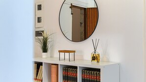 A room with a white console table, a mirror, a potted plant, a reed diffuser, and bookshelves with books. - Appartamento Monteverde Casa Marí Roma (Roma)