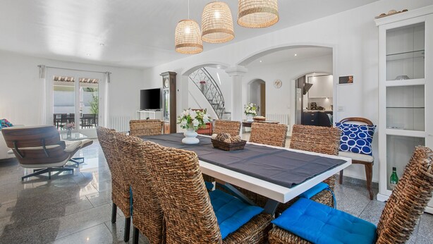 Uma sala de jantar espaçosa com móveis de vime, uma mesa grande e luminárias de vime suspensas.