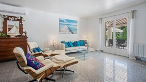 Uma sala de estar ampla com sofá, cadeiras, mesa de centro, um quadro e vista através de uma porta de vidro.