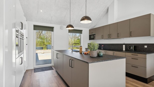 Une cuisine moderne dotée d’un îlot central, d’appareils électroménagers intégrés et de luminaires suspendus.