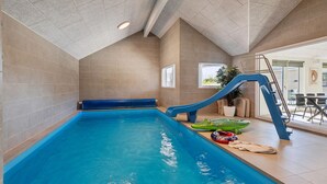 Une piscine intérieure avec un toboggan, une échelle et une vue sur l’extérieur.
