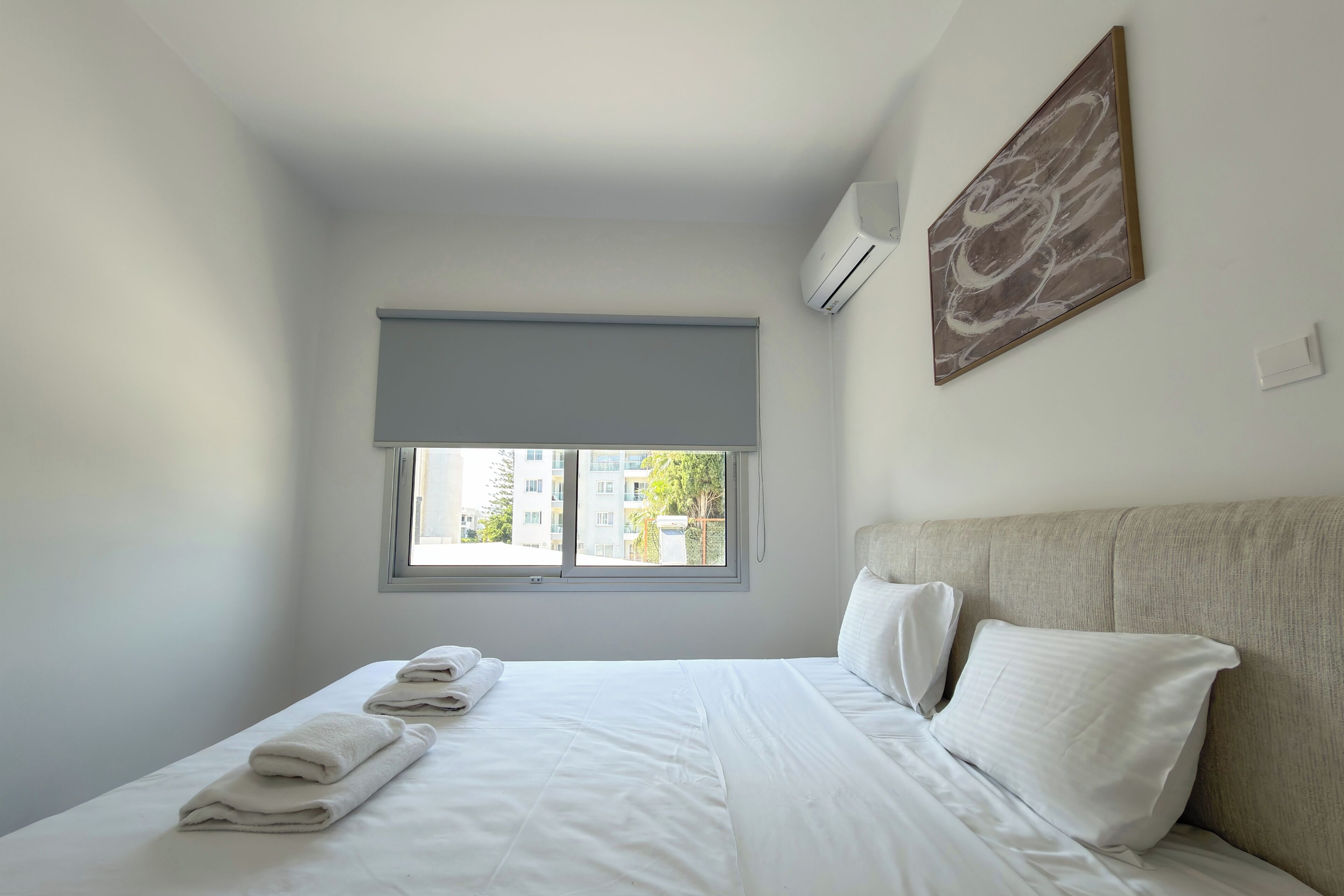 Habitación de hotel con cama, ventana con vistas, aire acondicionado y un cuadro en la pared.