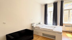 Ein schlicht eingerichtetes Schlafzimmer mit einem Bett, einer schwarzen Couch und einem Fenster mit Vorhängen.
